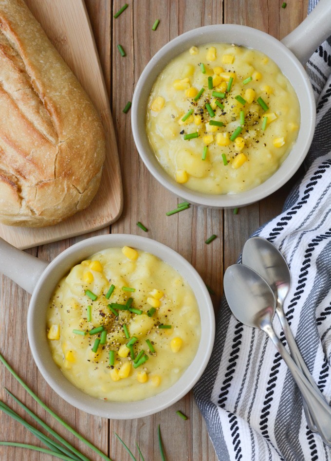 2 bowls of thick and cream Vegan Potato Corn Chowder. They're topped with fresh green onion and black pepper. Served with a sourdough bread loaf.
